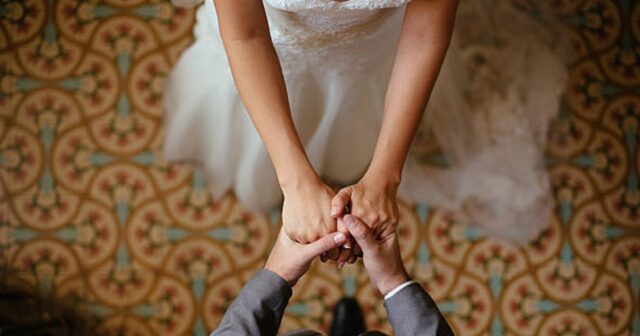 A close up shot of a bride and groom holding hands from a top view.