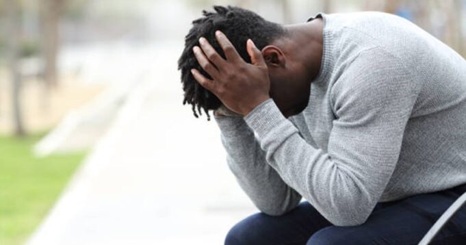 Side view portrait of a sad depressed black man sitting on a bench in a park